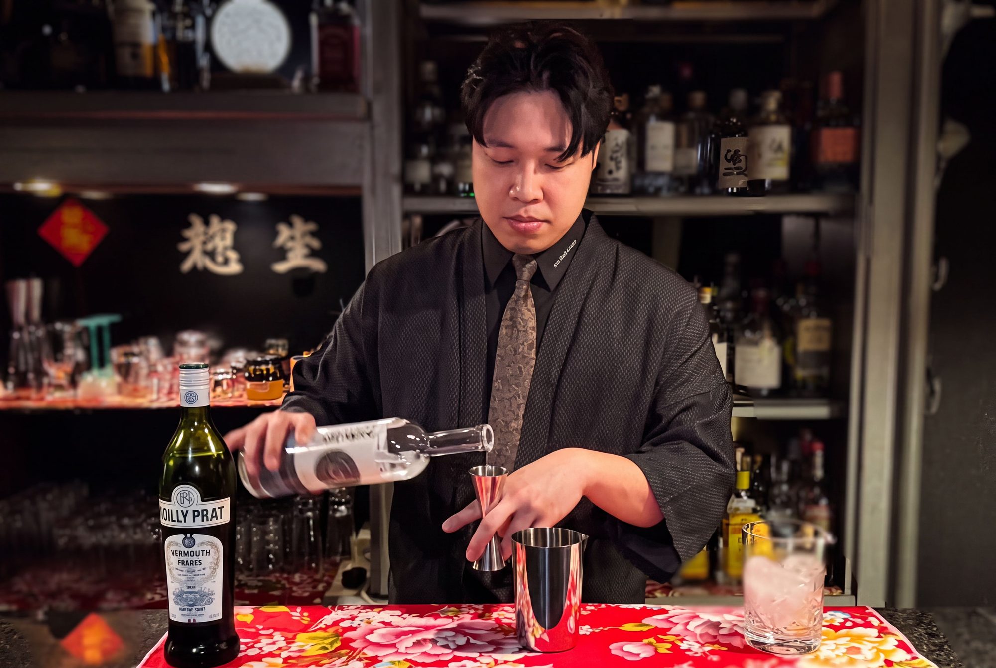 A bartender in a black haori pouring a measure